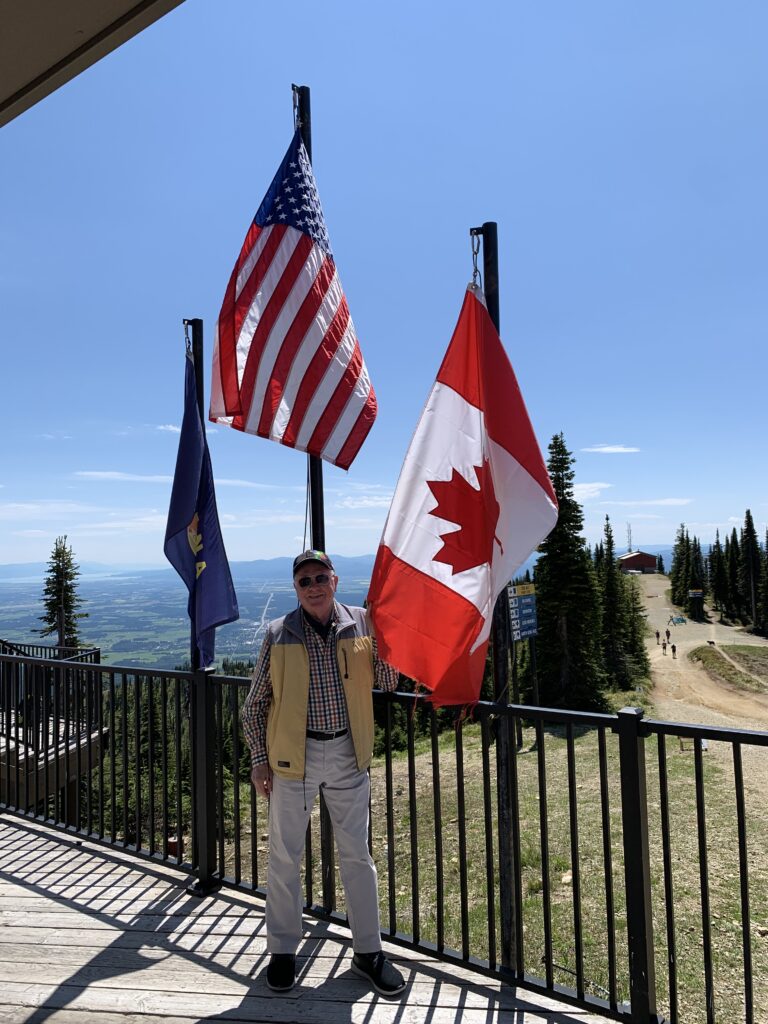 A senior man standing in front of the USA and Canada flag