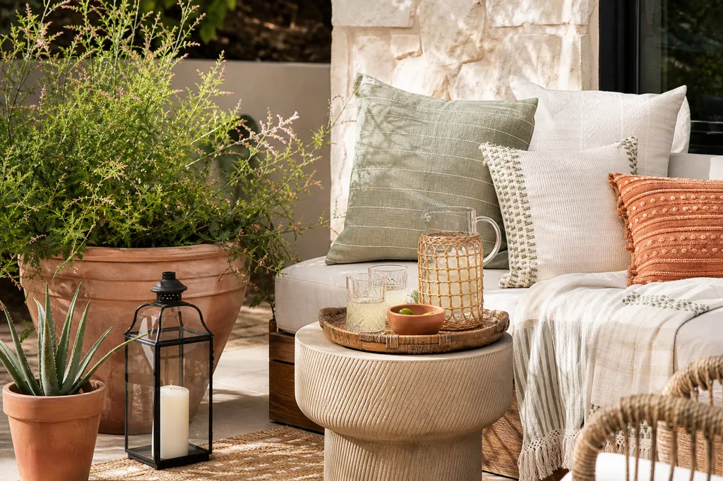 Close-up of a styled patio corner with layered textiles, a lantern, and potted plants