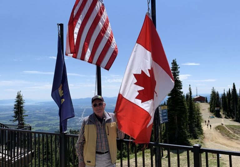 A senior man standing in front of the USA and Canada flag